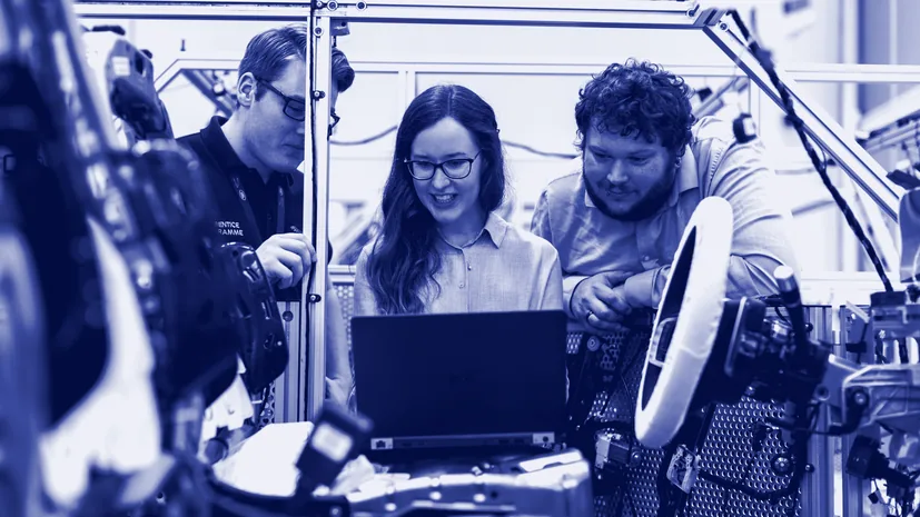Three people looking at a laptop beside factory equipment